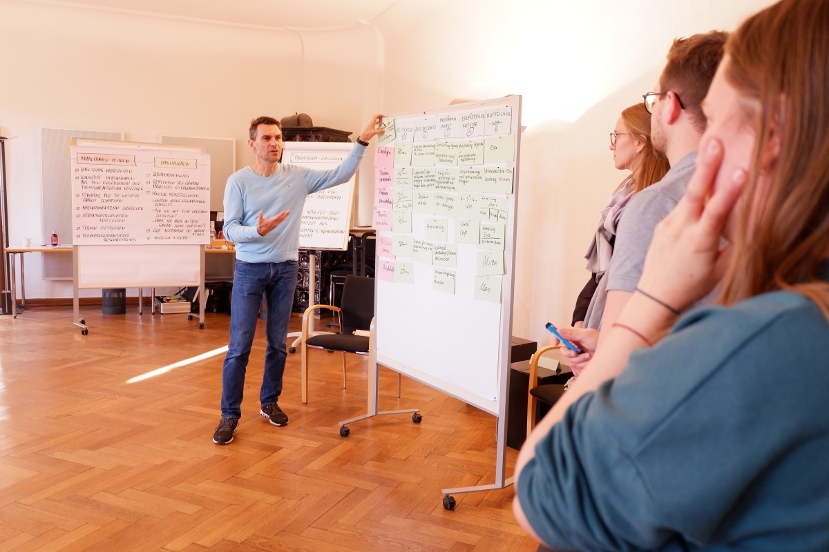 Der Moderator Markus Gebhardt im Seminar Moderationstraining an der SDL Thierhaupten an einer Pinnwand, Teilnehmer/-innen hören zu